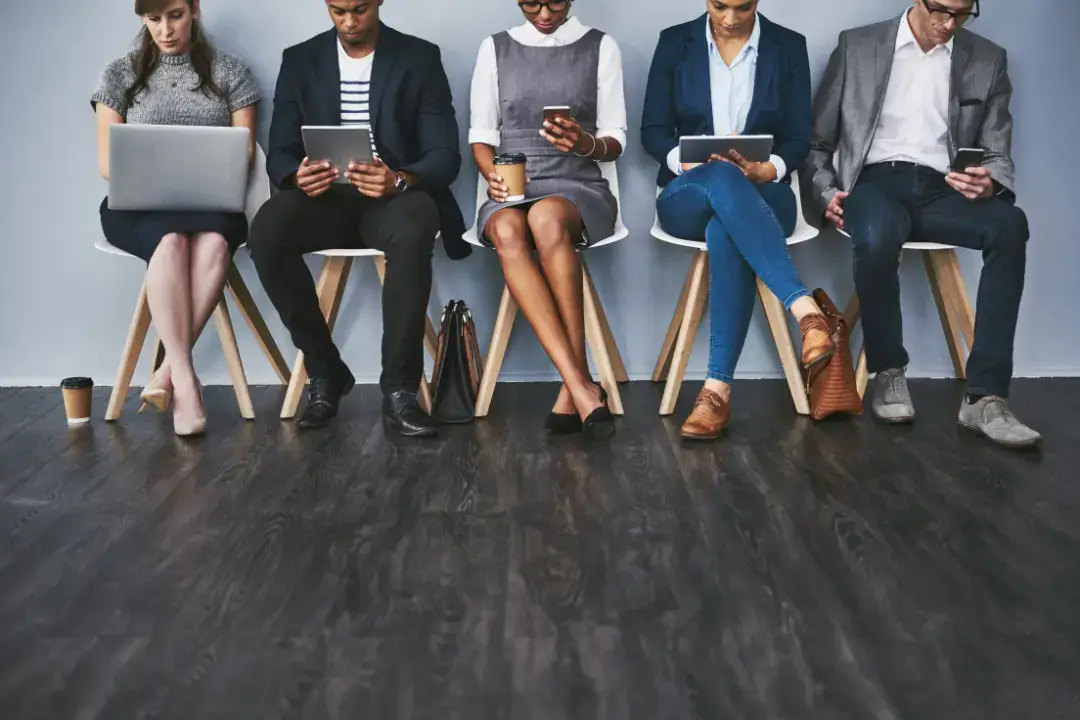 Diverse group using devices, waiting together.