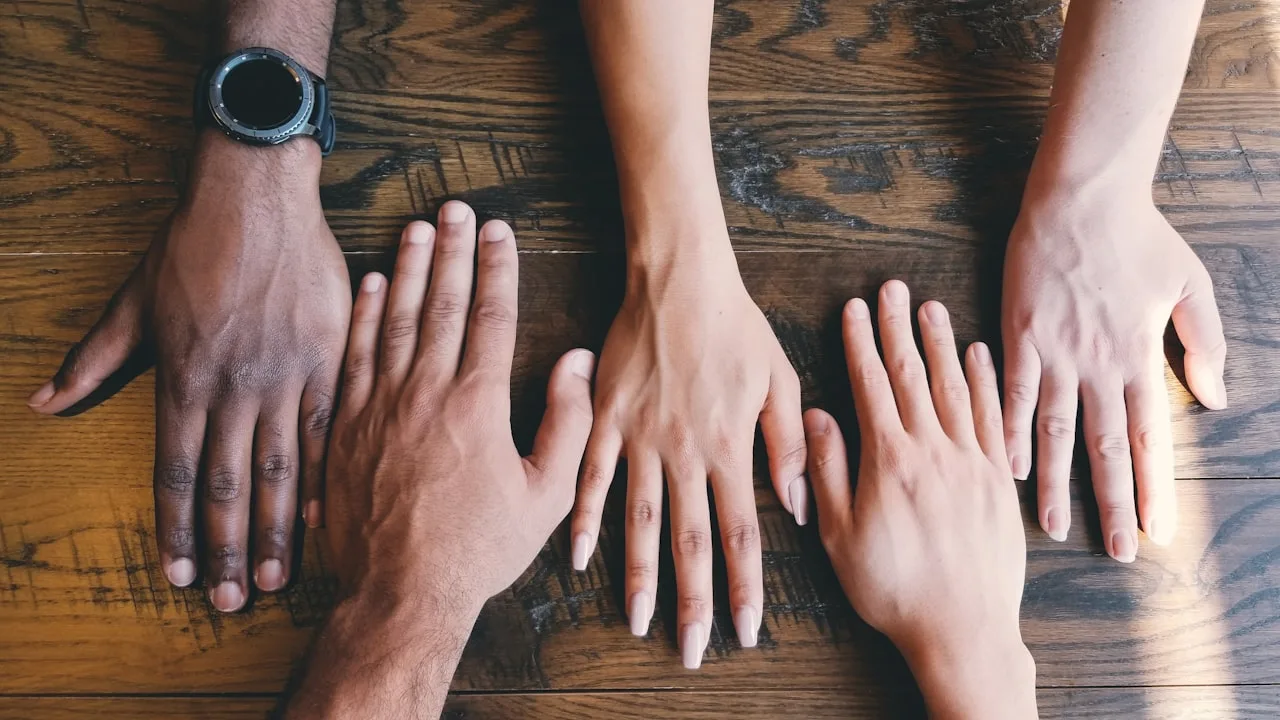 Five hands placed on a wooden table